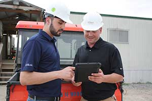 Two men wearing hardhats looking at a tablet